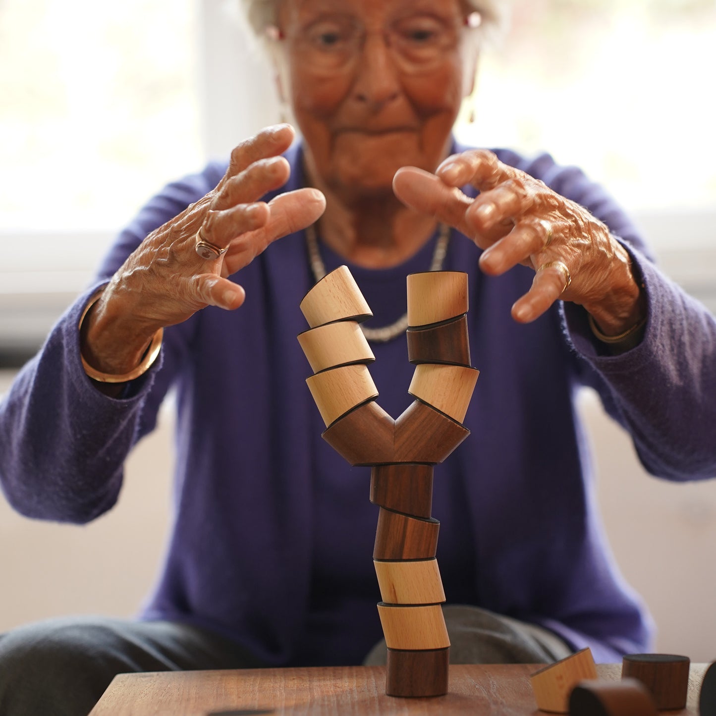 Eine Seniorin spielt mit dem Loggos Stapelspiel aus Buchen- und Nussholz