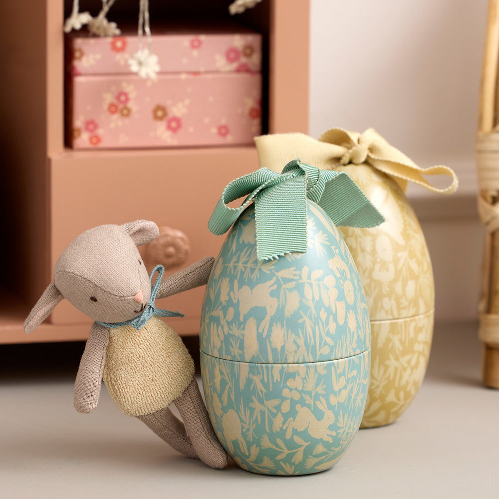 Moodbild mit kleinem Lamm in weißem Strick-Overall und blauer Schleife, liebevoll an zwei Ostereiern platziert