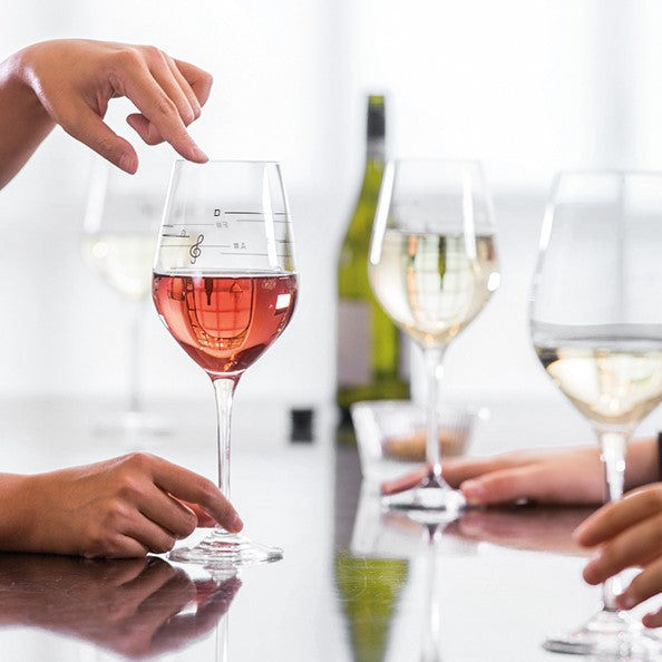 Drei Weingläser mit Roséwein auf einem Tisch, eine Person erzeugt durch Berühren des Glasrands Töne.