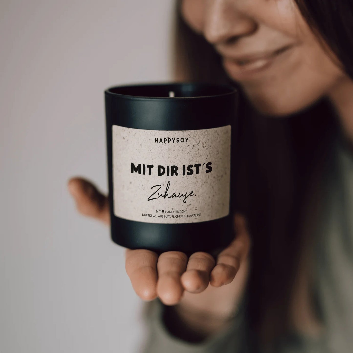 Jemand hält schwarze HappySoy Kerze mit liebevollem Schriftzug ‘Mit dir ist's zuhause’