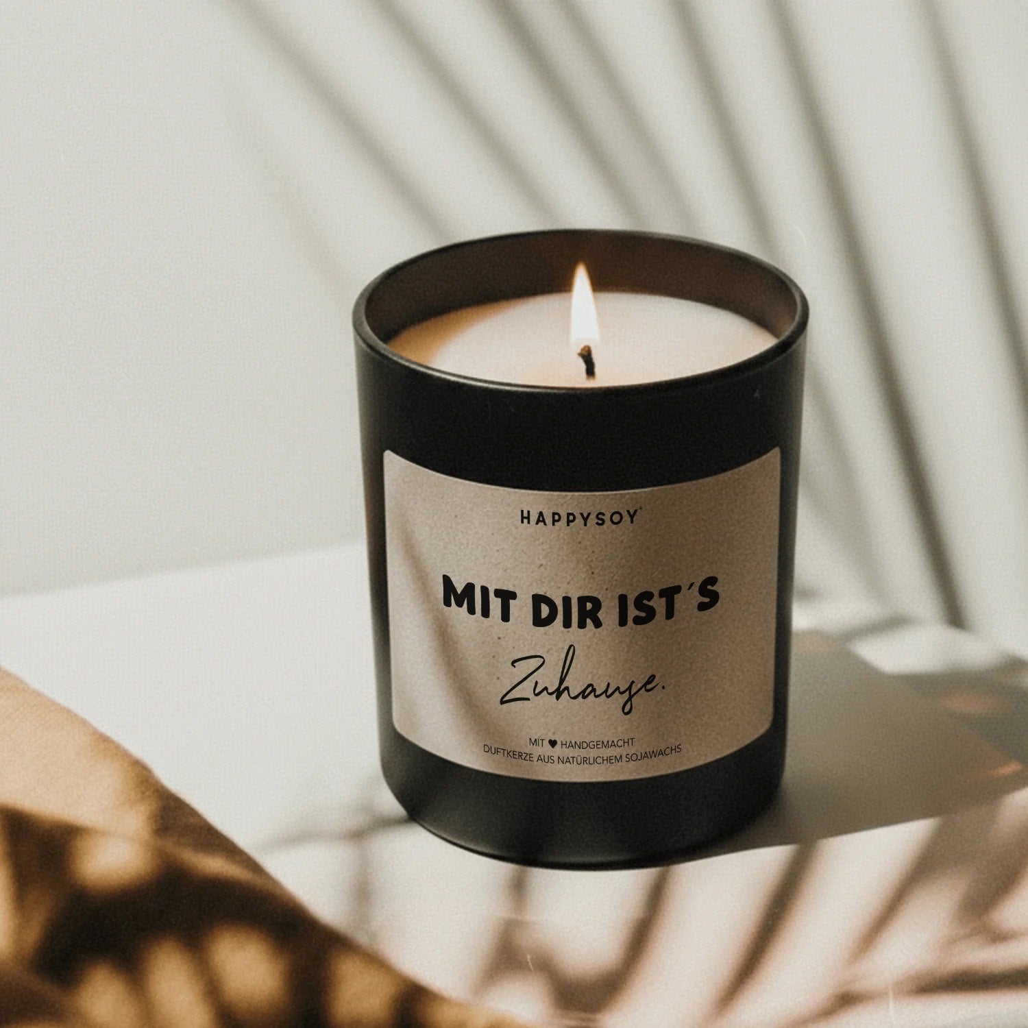 Angezündete schwarze Sojawachskerze von HappySoy mit Spruch ‘Mit dir ist's zuhause’