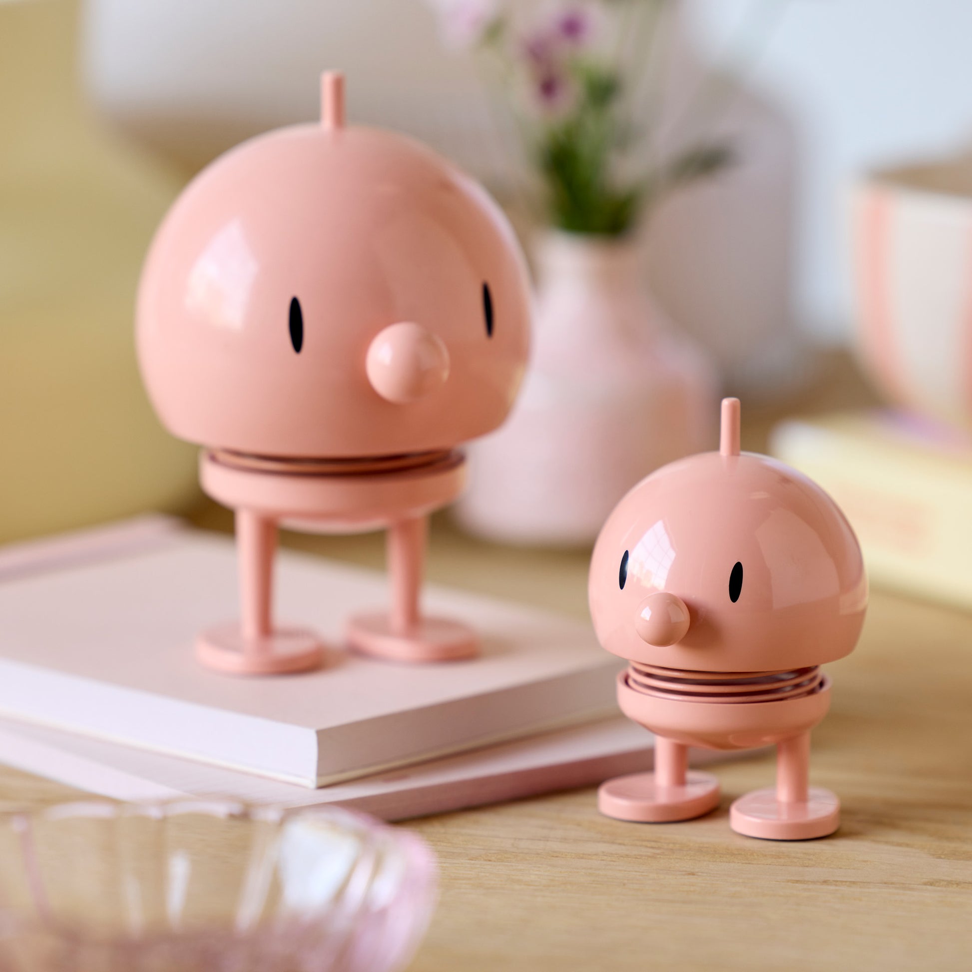 Small und Medium Hoptimist Bumble Figuren in Melon nebeneinander arrangiert, beide rund und glänzend mit freundlichem Gesicht und sichtbarer Feder als Wackelmechanismus