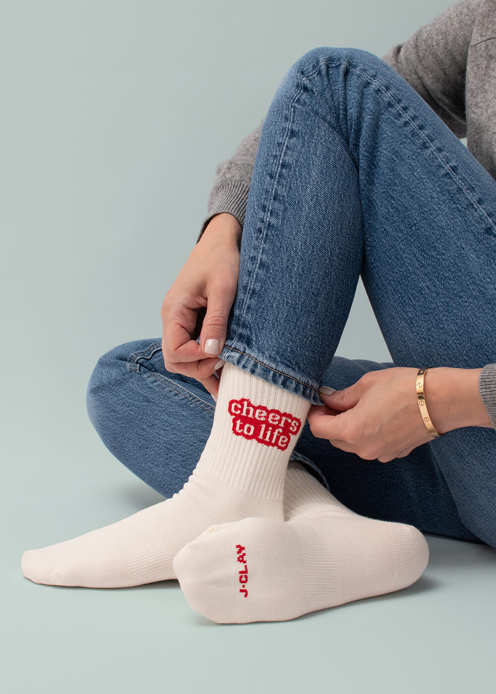 Weiße Crew-Socken mit rotem „Cheers to Life“-Schriftzug, kombiniert mit Jeans