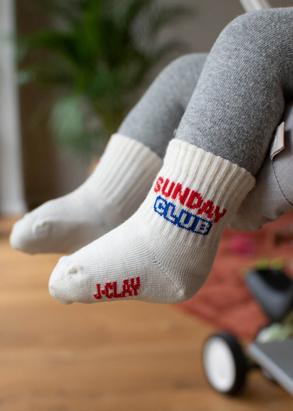 Weiße Babysocken mit „Sunday Club“-Schriftzug, getragen von einem Baby