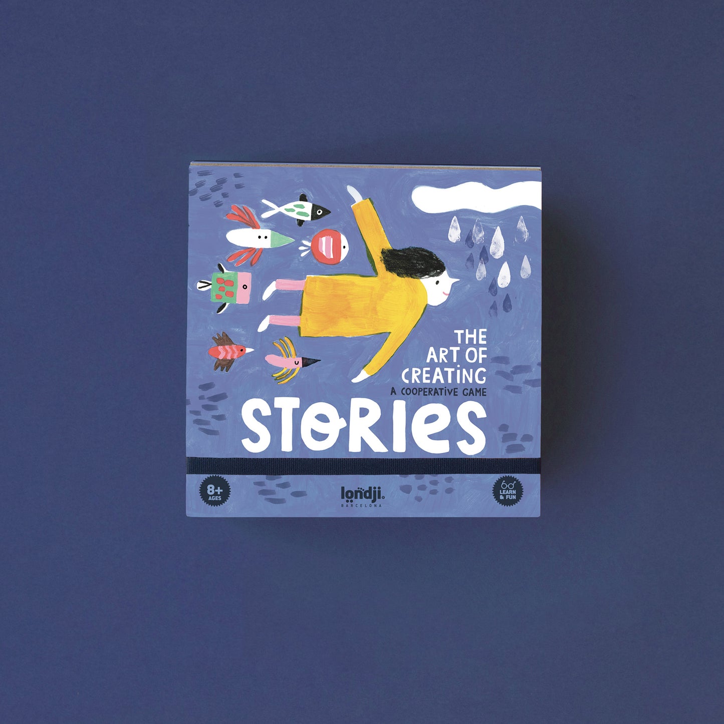 Spiel „Stories“ von Londji, blaue Spielbox mit Illustration eines Mädchens im gelben Kleid im Wasser, umgeben von Fischen