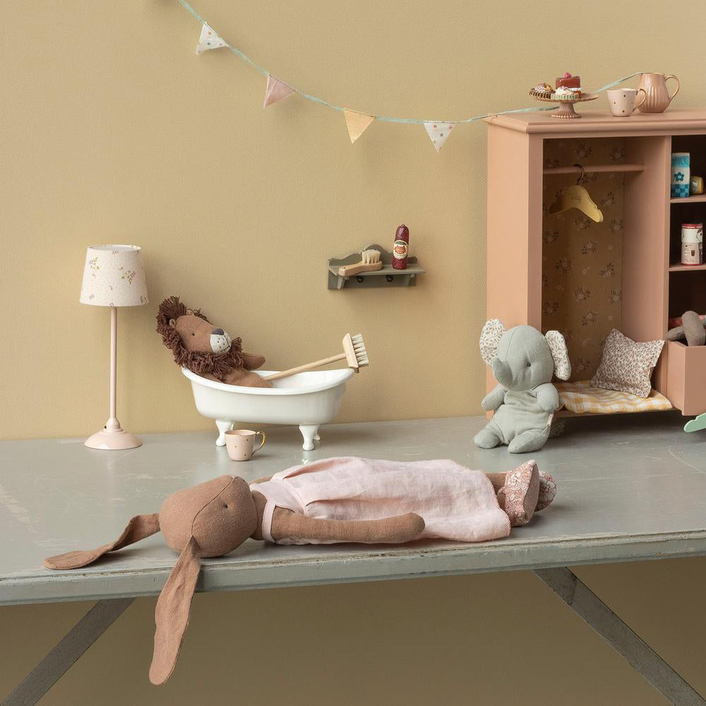 Schokoladenbrauner Stoffhase liegt auf dem Boden, ein Stofflöwe sitzt in der Badewanne, stimmungsvolle Szene mit weiteren Stofftieren im Zimmer