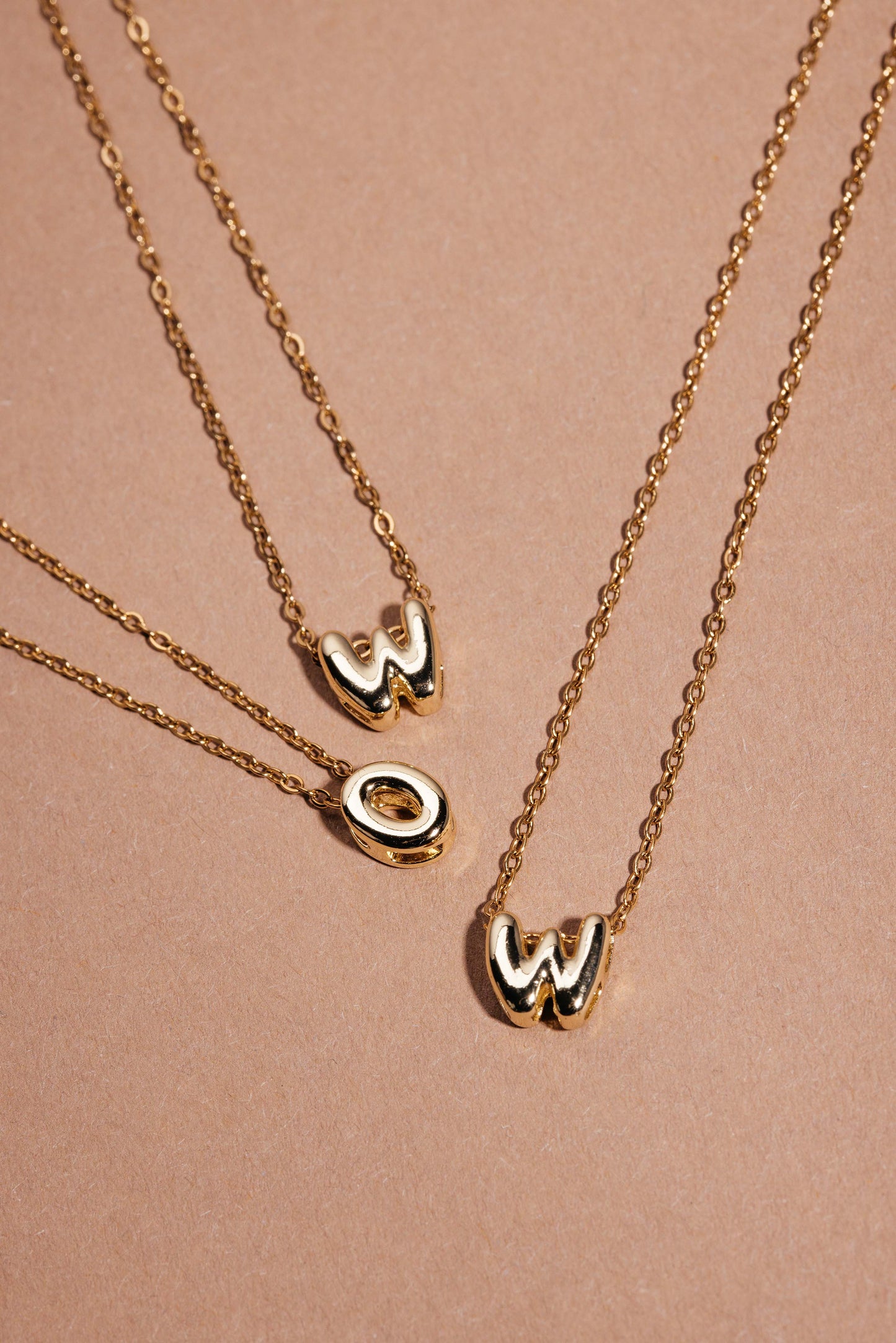 Drei goldene Ketten mit Bubble-Letter-Charms W, O und W, so angeordnet, dass sie ‚WOW‘ bilden