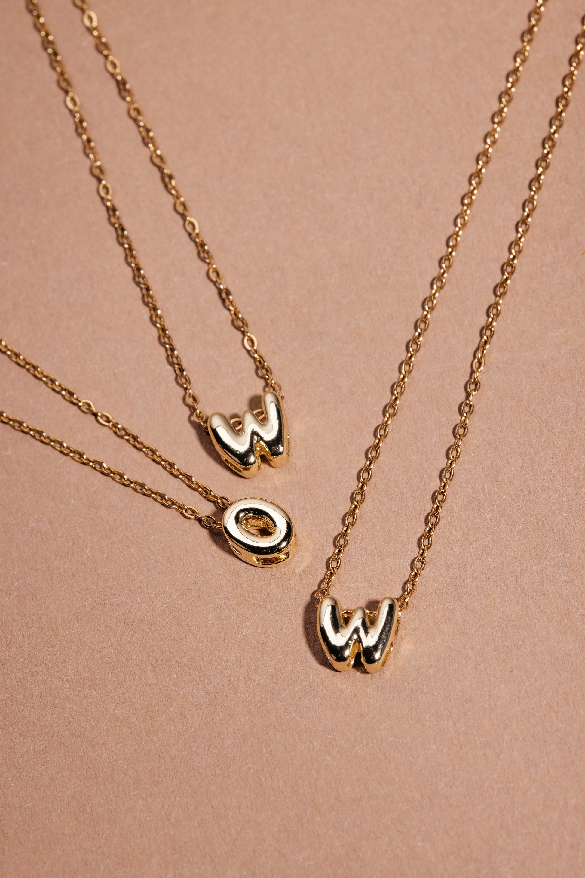 Drei goldene Ketten mit Bubble-Letter-Charms W, O und W, so angeordnet, dass sie ‚WOW‘ bilden