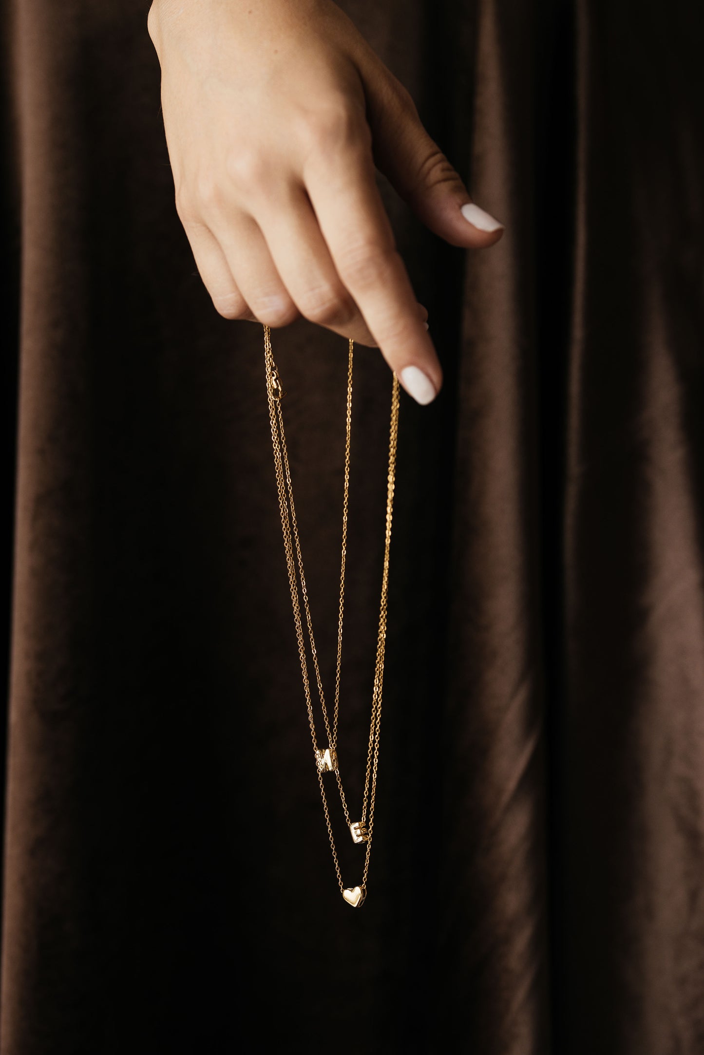 Hand hält drei goldene Ketten mit den Charms M, Herz und E