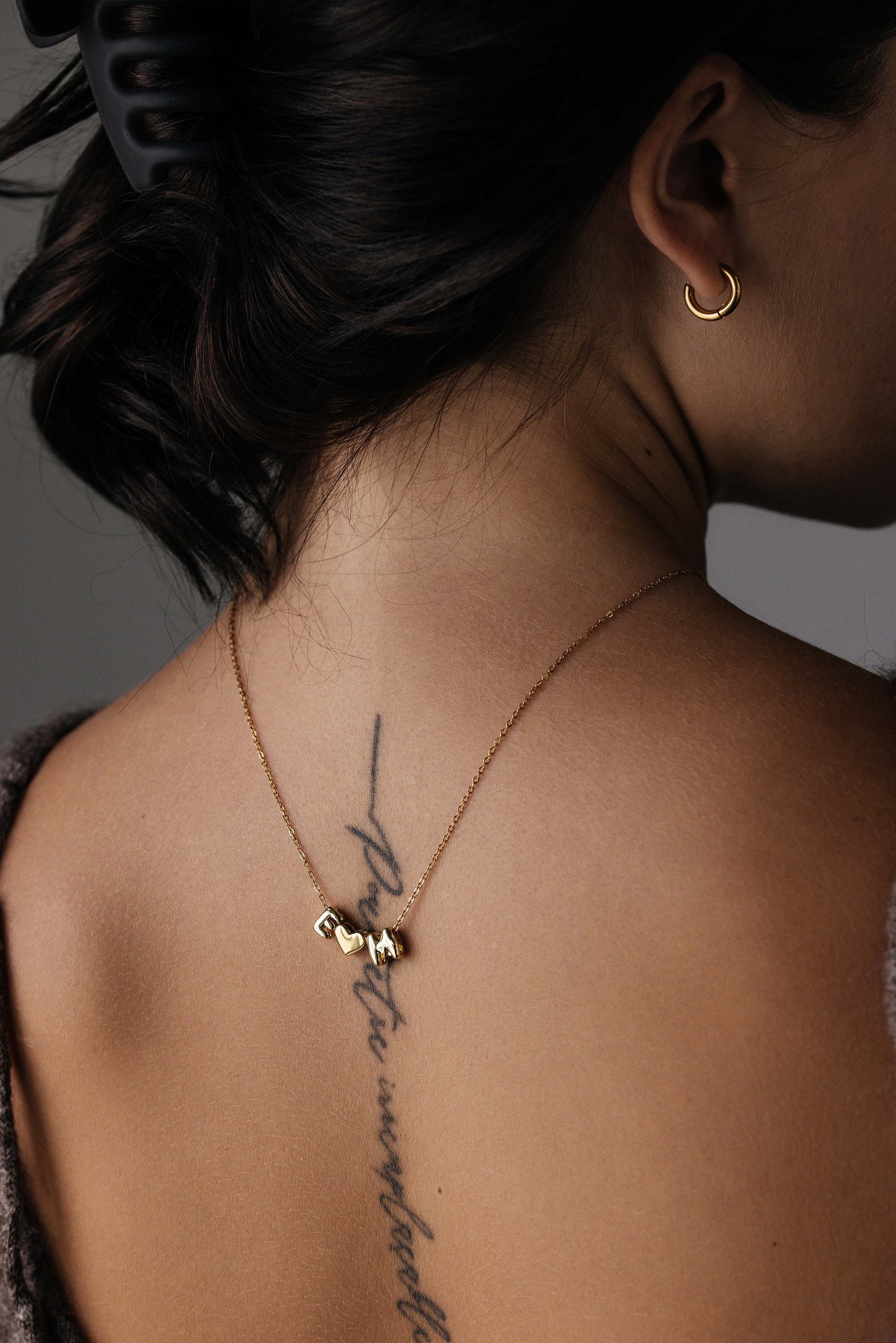 Rückwärts getragene goldene Kette am Rücken mit den Buchstaben E, Herz, M