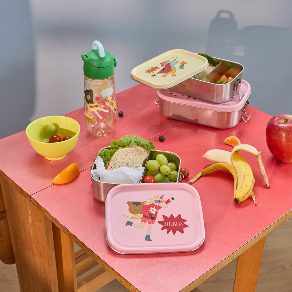 Zwei Edelstahl-Lunchboxen mit gelbem und rosa Deckel, mit Superhelden-Motiven, geöffnet und mit Snacks gefüllt, auf einer Picknickdecke als Moodbild