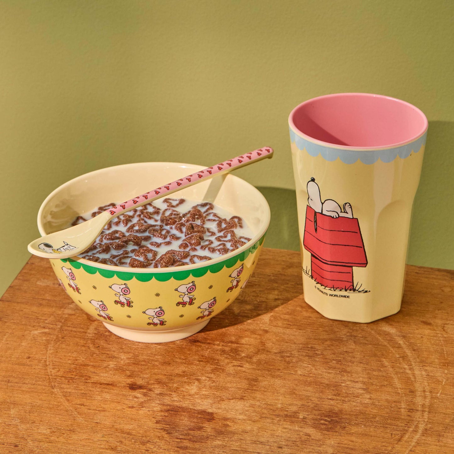 Melaminbecher und passende Schüssel von rice im Snoopy-Design, liebevoll nebeneinander arrangiert, wobei die Schüssel mit frischem Müsli gefüllt ist und eine gemütliche, verspielte Frühstücksszene entsteht