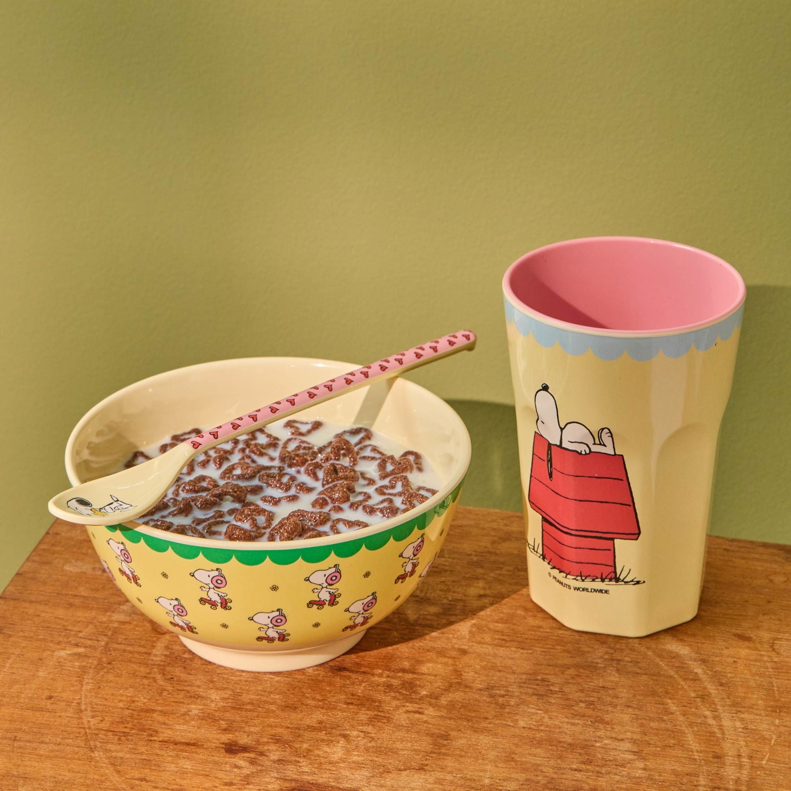 Melaminbecher und passende Schüssel von rice im Snoopy-Design, liebevoll nebeneinander arrangiert, wobei die Schüssel mit frischem Müsli gefüllt ist und eine gemütliche, verspielte Frühstücksszene entsteht