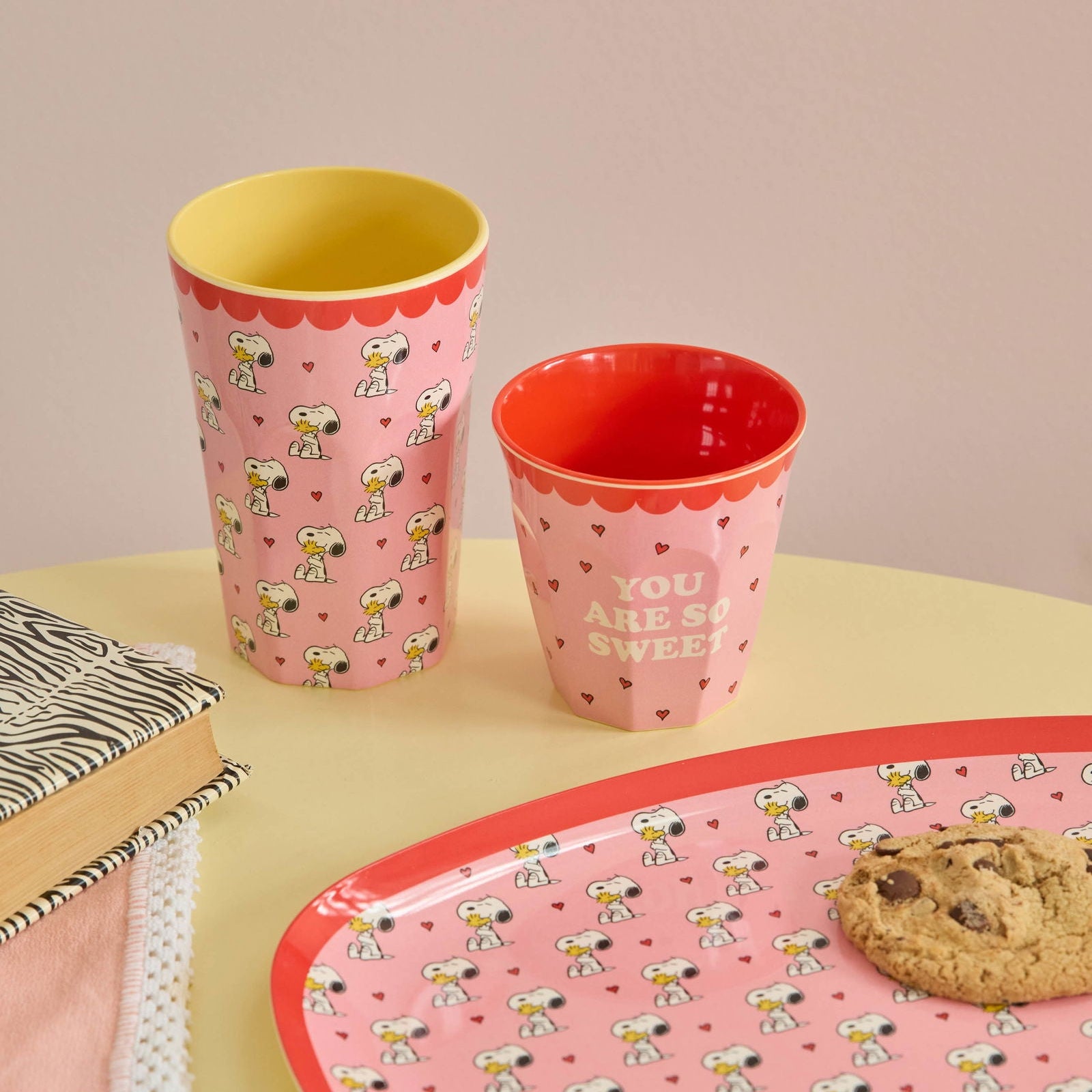 Moodbild mit einem großen und einem kleinen Melaminbecher im Snoopy-Design sowie einem passenden Teller, liebevoll arrangiert in harmonischen Farben für eine fröhliche, verspielte Tischszene