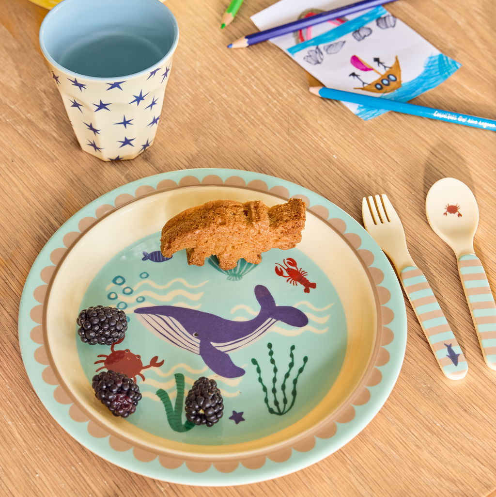 Moodbild mit blauen Kinderbesteck  zusammen mit passendem rundem Kinderteller im Ocean Design, liebevoll arrangiert auf gedecktem Tisch