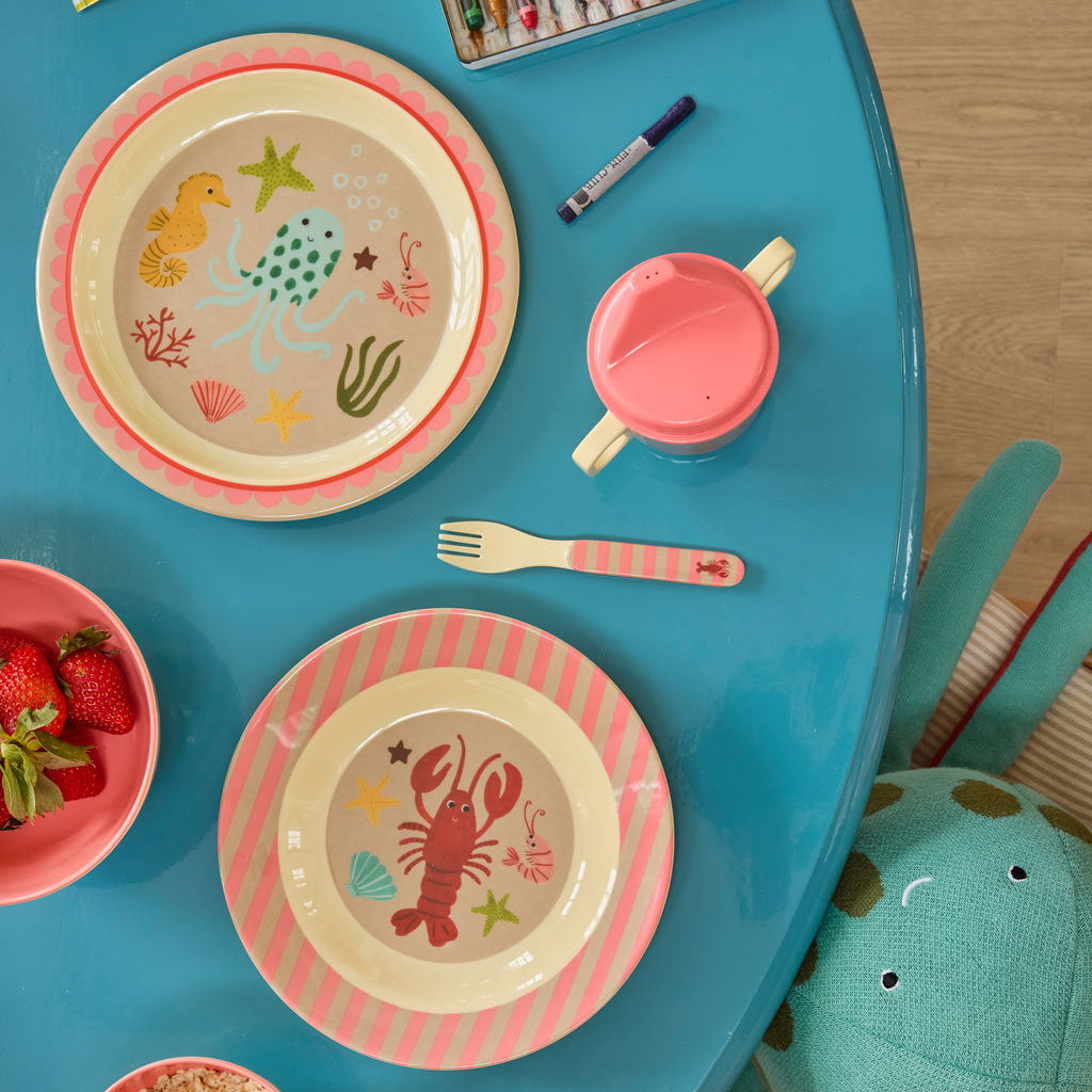 Melamin-Teller von Rice mit Ocean-Motiv, kombiniert mit Besteckset in Koralle, dekorativ auf einem Esstisch arrangiert