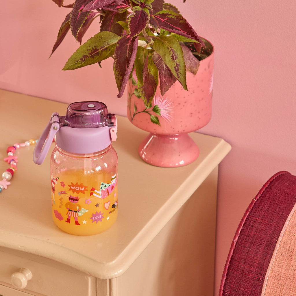 Lila Trinkflasche als Moodbild, mit Orangensaft gefüllt und auf einer Kommode arrangiert